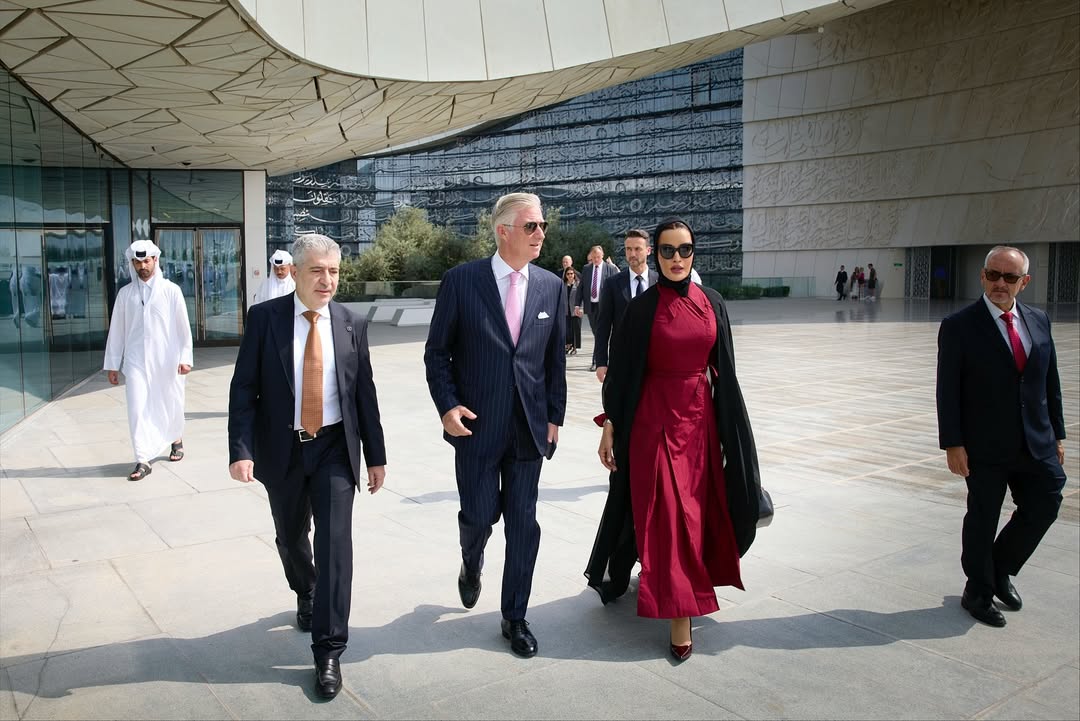 أثناء زيارة الملك فيليب، ملك بلجيكا، إلى مقر مؤسسة قطر وجامعة حمد بن خليفة، ظهرت سمو الشيخة موزا بنت ناصر بإطلالة أنيقة عكست الدقة في التفاصيل التي أتت مكملة لبعضها البعض.   الشيخة موزا بفستان بتصميم مخصص لها مع عباية سوداء  ارتدت الشيخة موزا فستان بتصميم خاص من المصمم الإسباني خوان فيدال Juan Vidal، مستوحى من مجموعته لخريف 2019، تميز بياقة كلاسيكية على شكل قميص مع تعديلات واضحة في القصة لتناسب أسلوبها المحافظ والأنيق. الفستان جاء باللون الأحمر البوردو وبقصة ضيقة عند الخصر وتنورة واسعة قليلاً بثنيات واضحة منحت الإطلالة حركة متوازنة. نسّقت سموّها الفستان مع عباية شفافة ووشاح أسود، ما أضفى تبايناً هادئاً بين الأحمر العميق والأسود الكلاسيكي، كما اختارت نظارات شمسية سوداء أكملت بها المظهر العام بطريقة عملية ومعبّرة عن الثقة. أما الحقيبة فكانت من دار روجيه فيفييه Roger Vivier، من طراز Choc Me  المصنوعة يدويًا من الجلد الطبيعي الأسود بتصميم مجعّد ومشبك معدني ثلاثي الأبعاد. يبلغ سعرها نحو 3995 دولار، وتجمع بين الطابع العملي والتفاصيل الحرفية الدقيقة التي تشتهر بها الدار. في ما يخص الإطلالة الجمالية، اختارت سمو الشيخة موزة مكياجًا ناعمًا بلمسات برونزية دافئة، مع لون شفاه يعزز إشراقة البشرة ويكمل توازن الإطلالة.